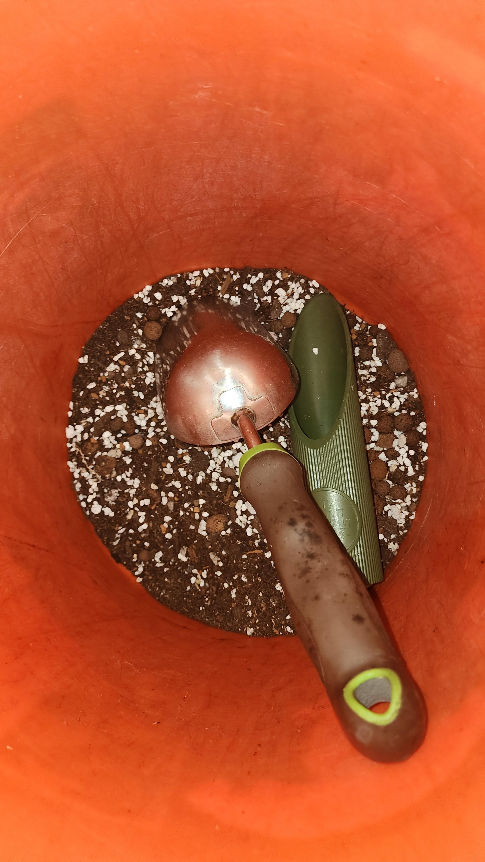 A brown-handled garden trowel and a green scoop rest in a large orange bucket filled with FAS Custom Soil-less Premium Mixes, an aroid soil blend of potting soil and white perlite designed to boost plant health.